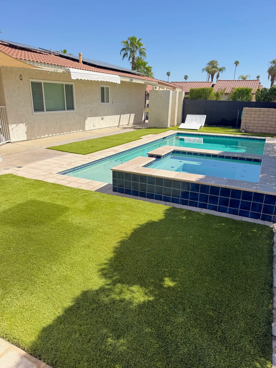 Artificial turf surrounding a backyard pool and raised spa with palm trees in Palm Desert