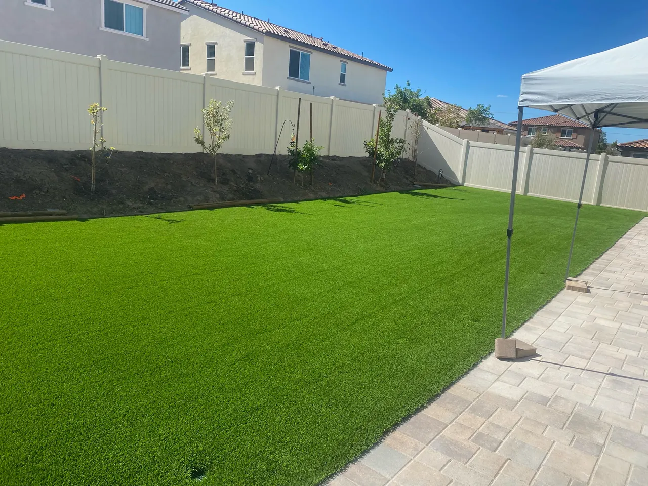 Artificial turf lawn alongside a paved patio, white fencing, and canopy in Culver City